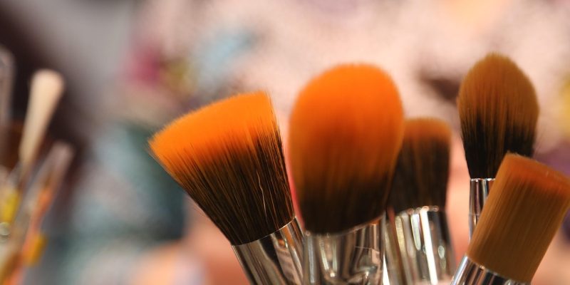 Orange and brown makeup brushes in a pot with a blurred background.